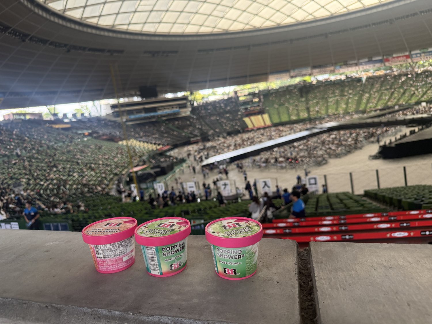 Three cups of Baskin-Robbins ice cream on a ledge, with the vast open-sided interior of Belluna Dome and daylight behind