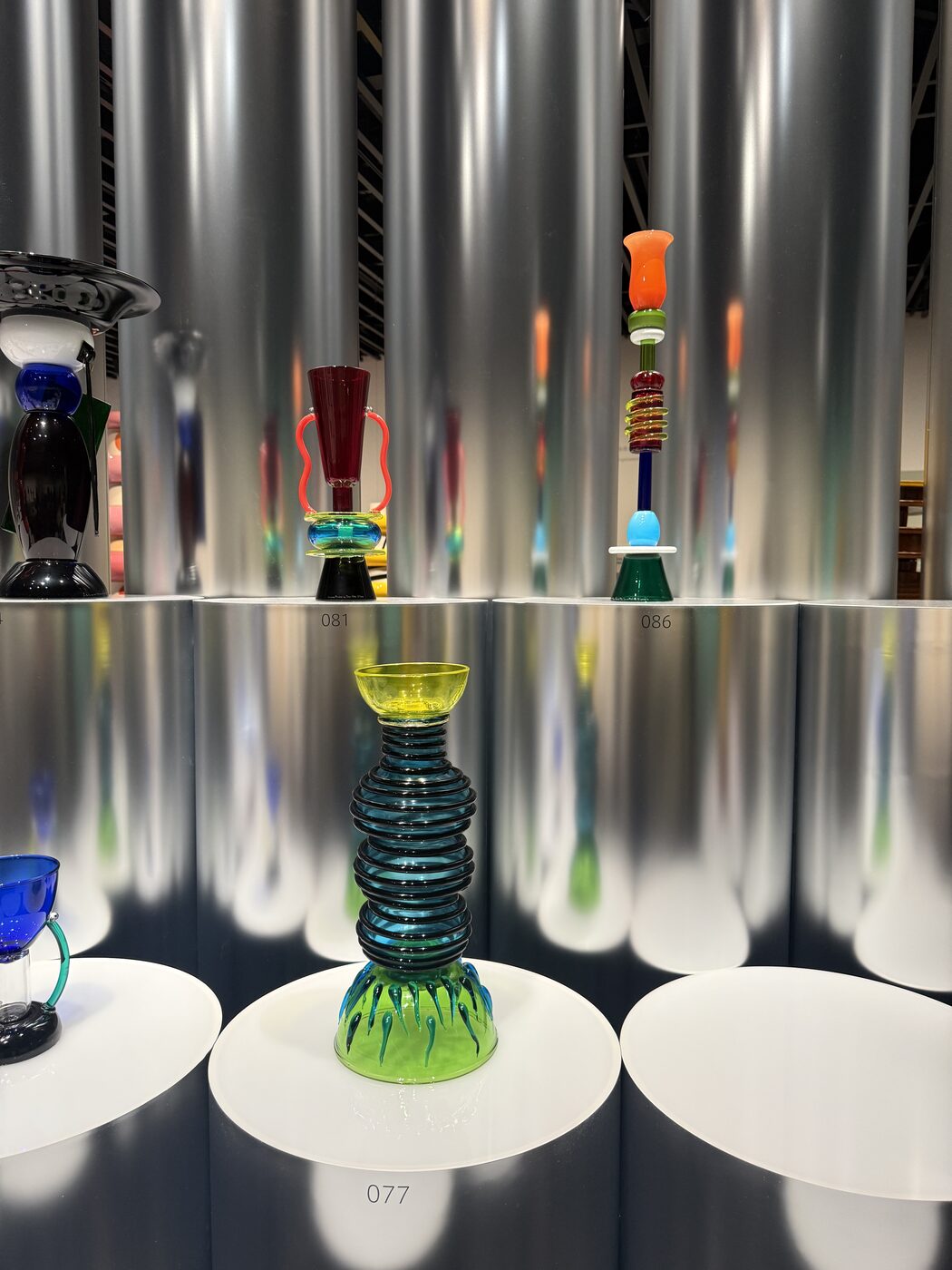 Brightly coloured Sottsass glass vases in a mirrored, lit display