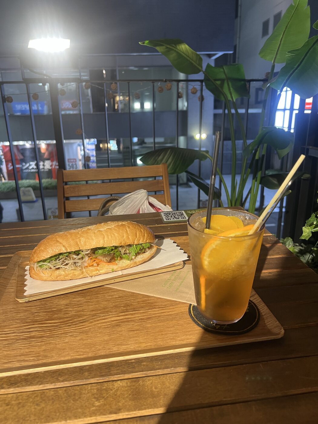 A filled Vietnamese banh mi and a citrus soda on a terrace table at night