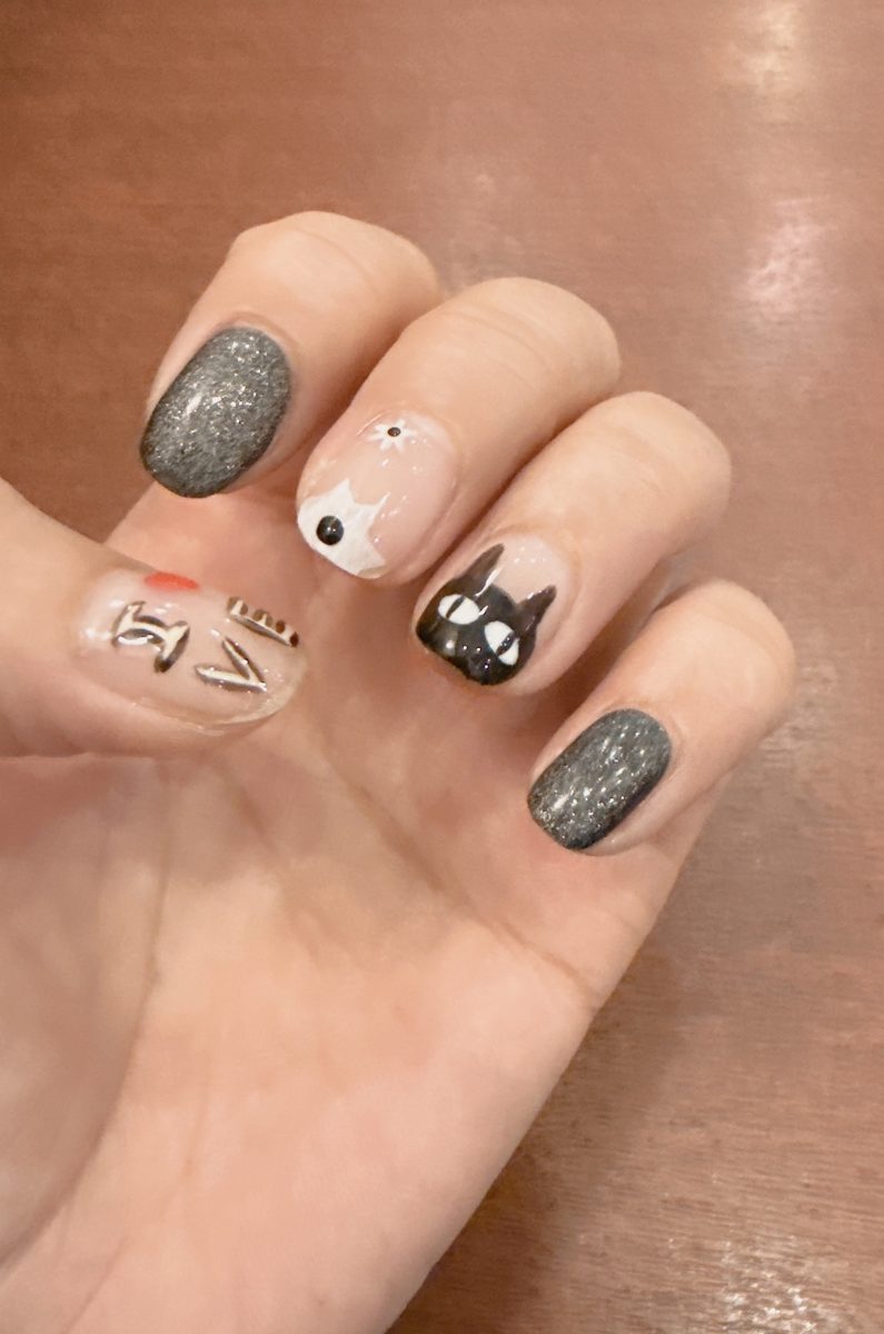 Short nails with dark grey shimmer gel on two fingers and hand-painted cat designs on the others