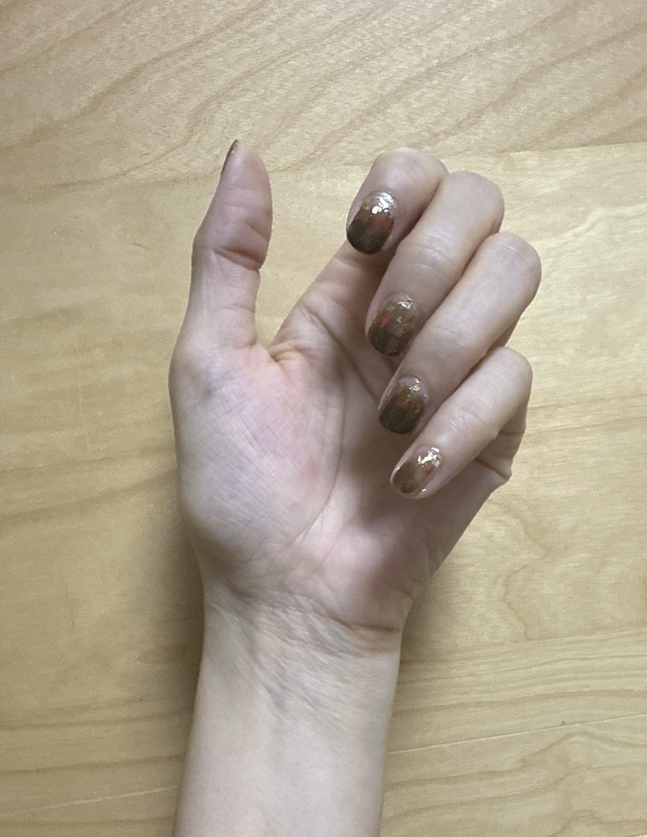 A hand with brown nails with darker gradient and small gold flakes