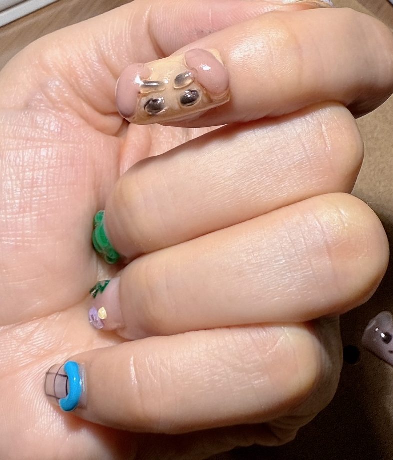 A hand with a puppy-face nail tip on the thumb and small colourful details on other nails