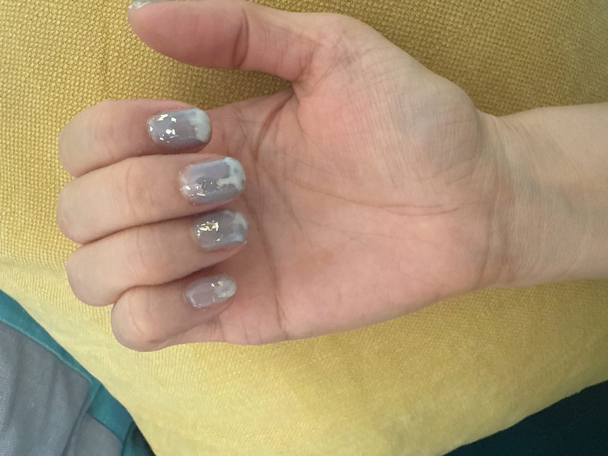 A hand with grey nails with white snowy tips and small gold flakes